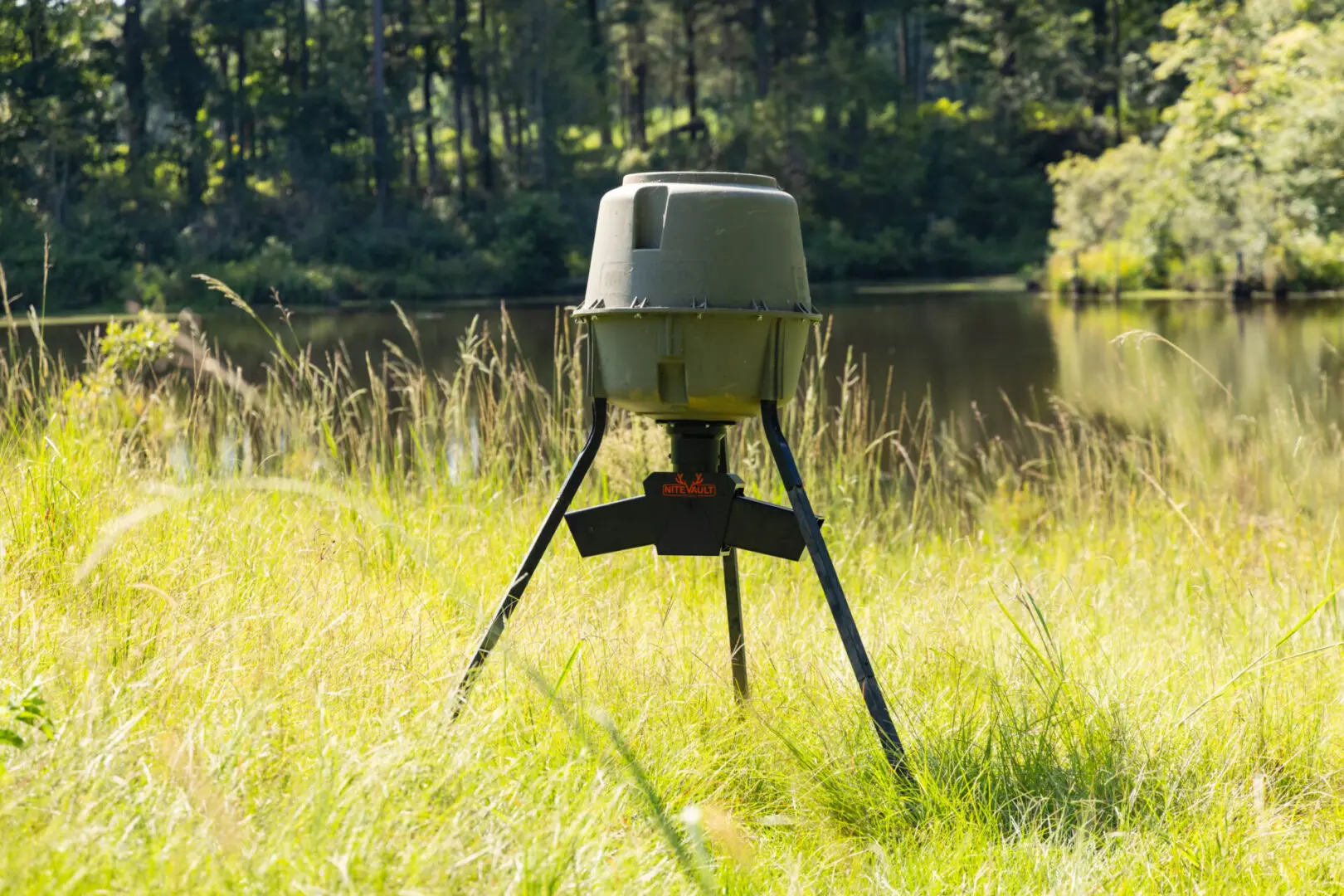 Here's an 8-word alt tag for the image: NiteVault deer feeder in grassy field near lake.